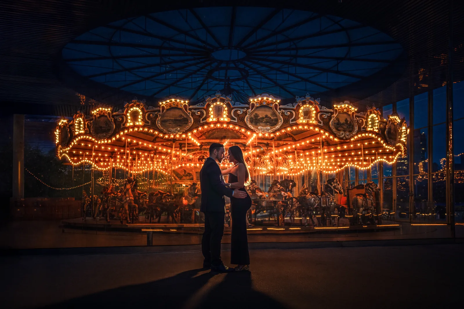 Engagement couple embracing in front of Jane's Carousel at night — George Pompilio Photography