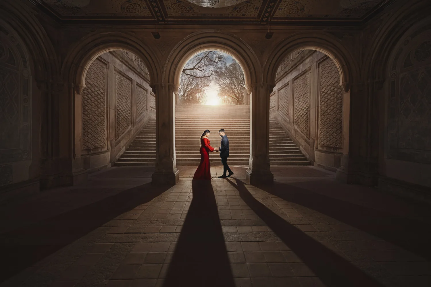 Groom-to-be in a dark tailored suit with his fiancée in a red gown in Central Park, engagement session by George Pompilio