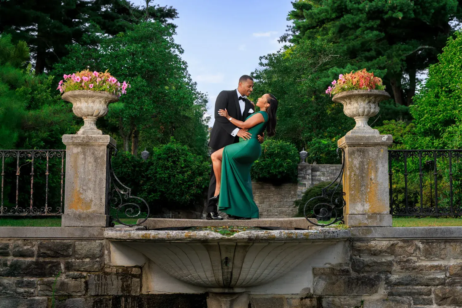 Couple in a dip pose on a stone garden terrace at Skylands Manor in Ringwood NJ, her emerald gown and heels lengthening the line of the pose, engagement session by George Pompilio