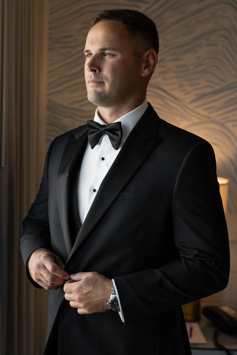 Luke buttoning his tuxedo jacket in window light before his wedding to Allison &mdash; George Pompilio Photography