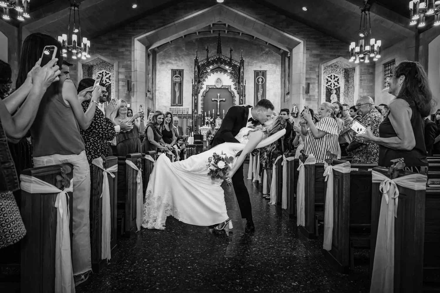Black and white dip kiss in the aisle as guests cheer at The Church of St. Christopher &mdash; George Pompilio Photography