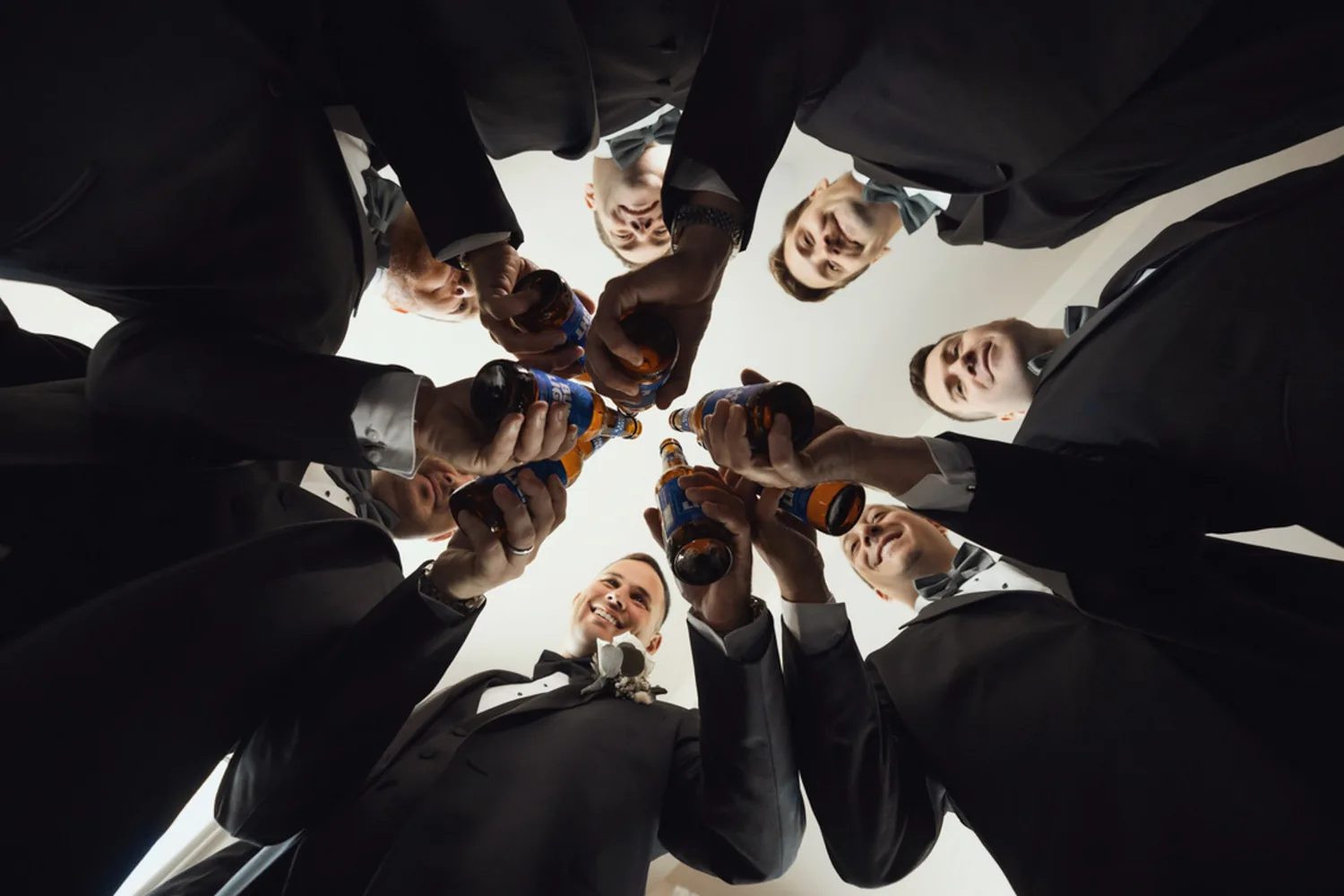 Luke and his groomsmen toasting with beers in a low-angle huddle while getting ready &mdash; George Pompilio Photography