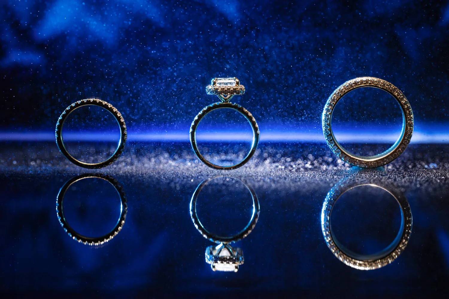 Chelsea and Ryan&rsquo;s wedding: Wedding rings on a reflective blue surface, Larkfield wedding detail &mdash; George Pompilio Photography