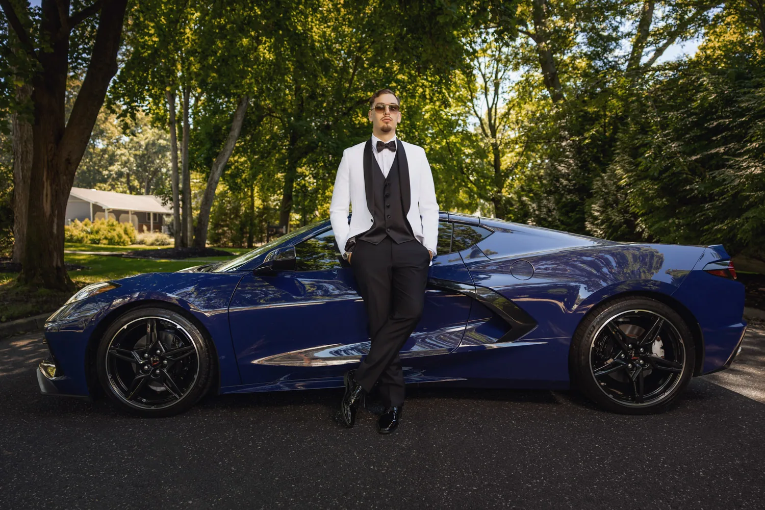 Ryan in a white tuxedo jacket leaning on his blue Corvette C8 before the wedding &mdash; George Pompilio Photography